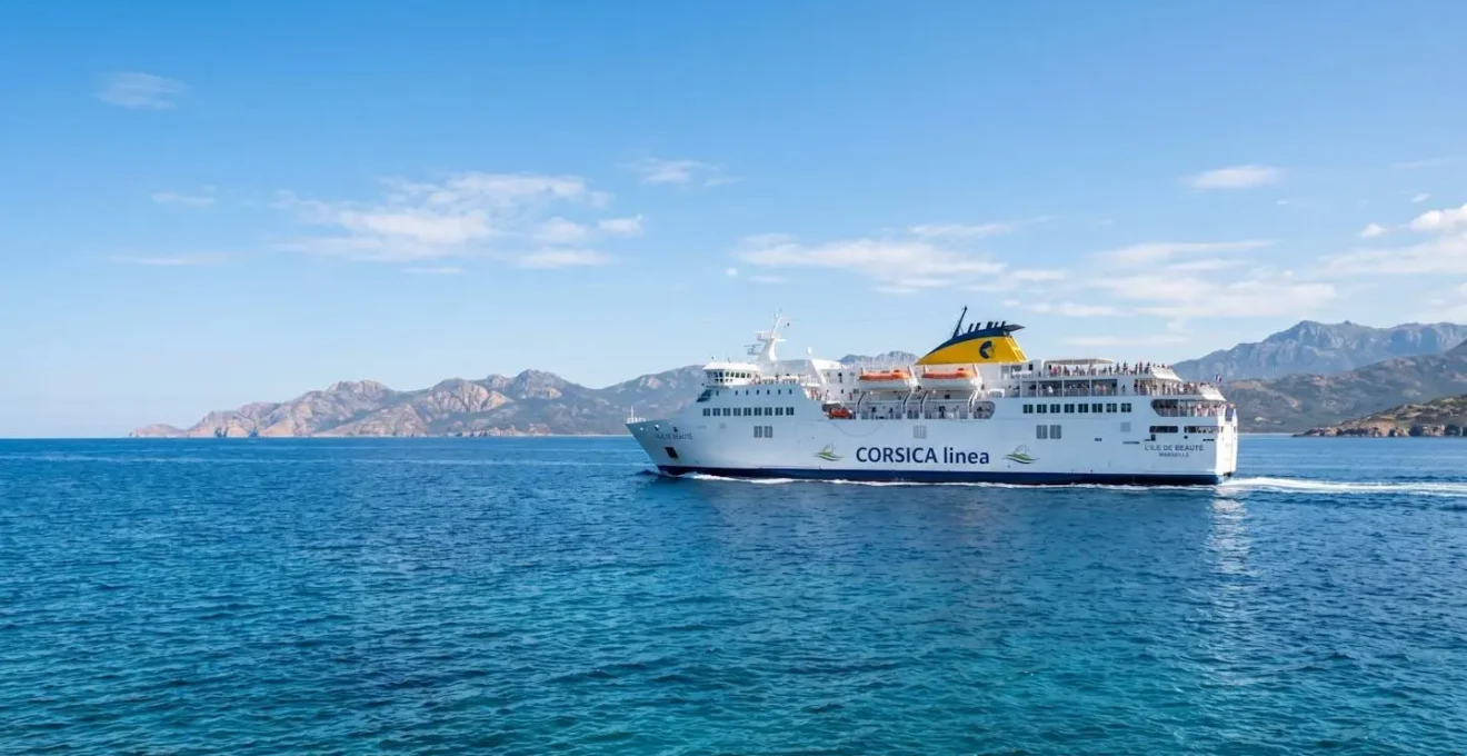 Un ferry blanc naviguant sur une mer Méditerranée calme et turquoise sous un ciel lumineux avec une côte visible au loin