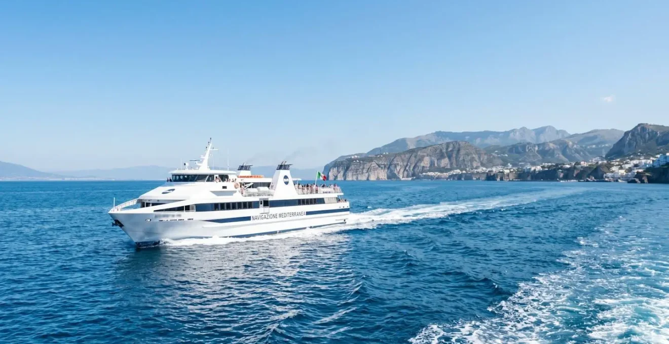 Un ferry blanc naviguant sur une mer Méditerranée calme et turquoise sous un ciel lumineux avec une côte visible au loin